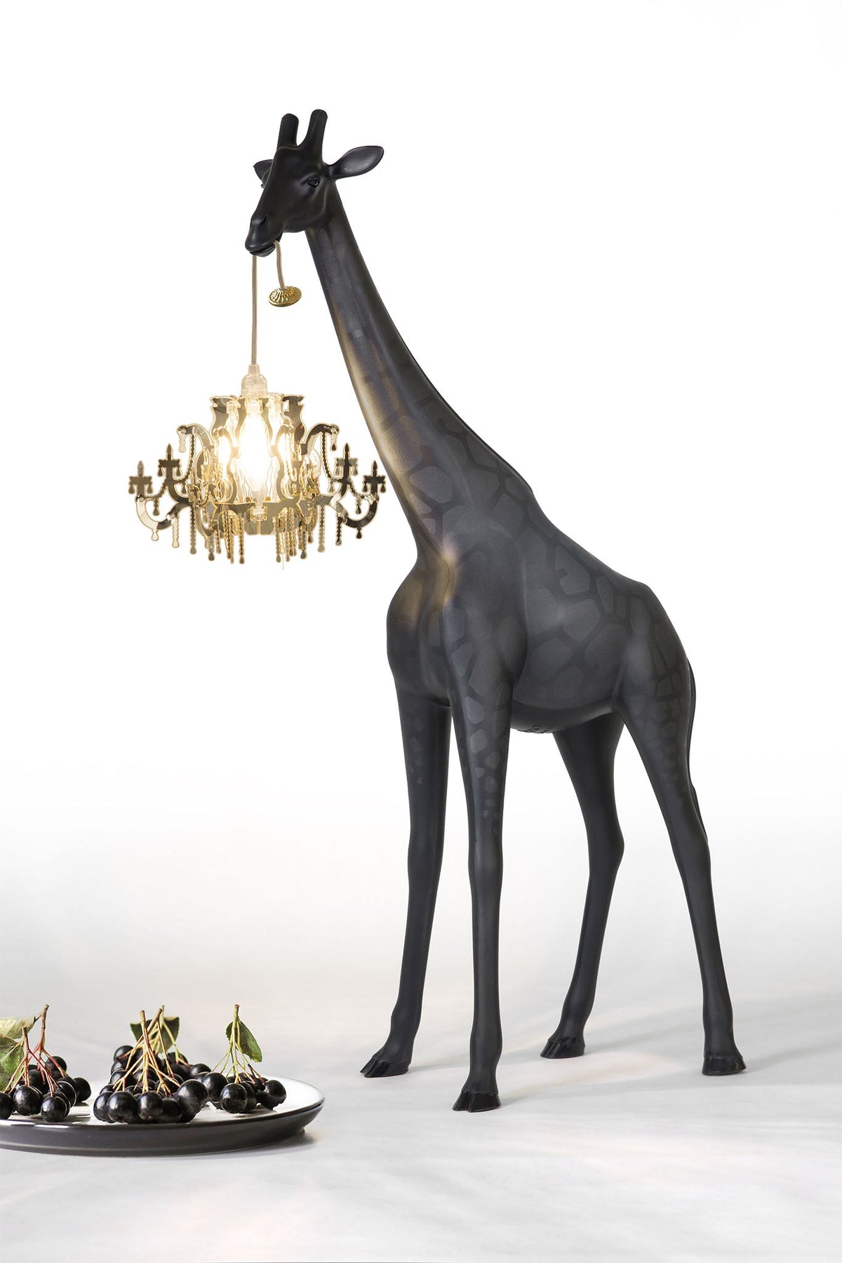 Stehleuchte GIRAFFE IN LOVE XS in schwarz mit Kronleuchter vor einem Teller mit Kirschen